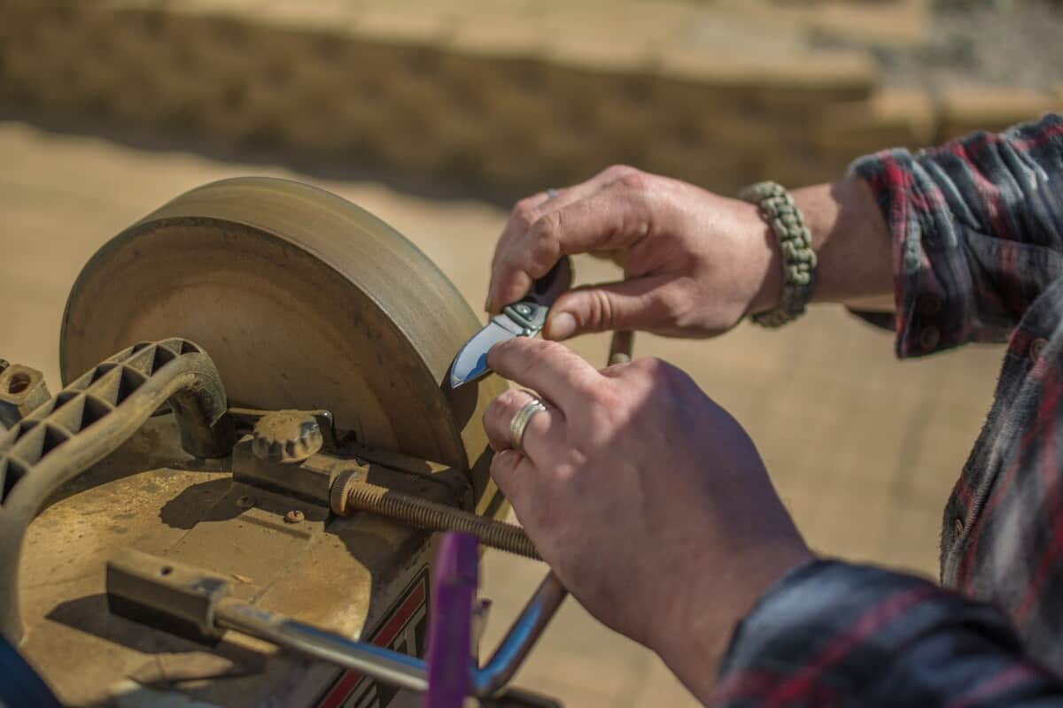 A hand sharpening a pocket knife blade against a grinding wheel outdoors