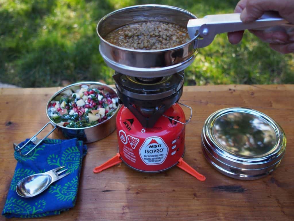 A pot of beans heating on a small canister-top camp stove set on a picnic table