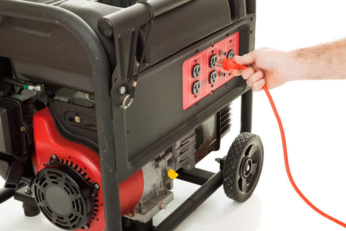 A close-up of a hand plugging an orange extension cord into the outlet panel of a portable gas generator