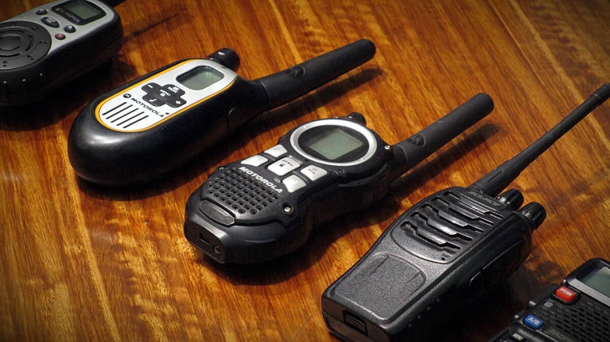 Four handheld two-way radios from different brands lined up on a wood table
