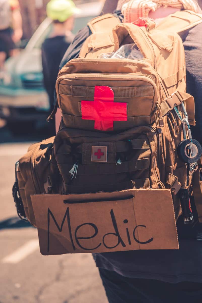 A homemade first aid backpack with a red cross patch and a cardboard "Medic" sign