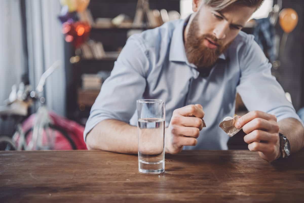 A man at a table unwrapping a water purification tablet next to a full glass of water