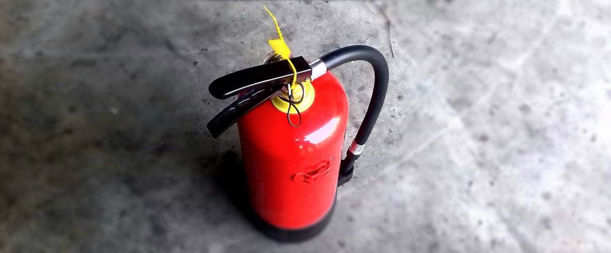 A red fire extinguisher with an intact tamper seal resting on a concrete floor