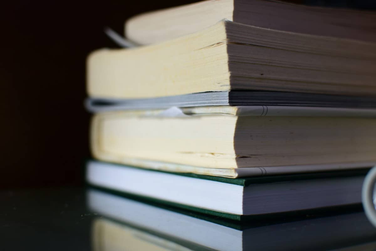 A stack of paperback and hardcover reference books on a dark reflective surface
